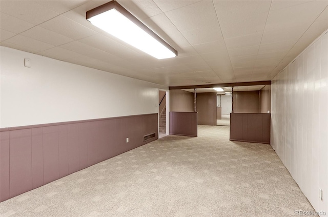finished basement featuring carpet, stairs, a wainscoted wall, and wooden walls