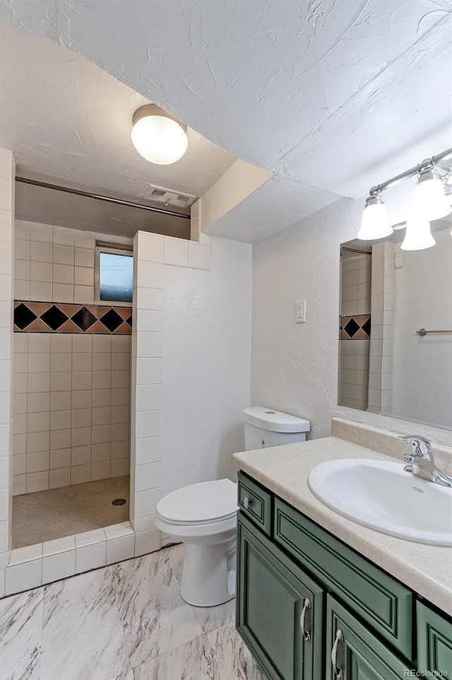 full bathroom with a tile shower, toilet, vanity, and marble finish flooring
