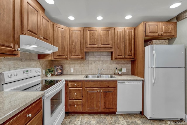 kitchen with backsplash, a sink, light countertops, under cabinet range hood, and white appliances