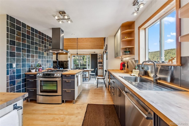 kitchen featuring a healthy amount of sunlight, butcher block countertops, wall chimney range hood, light wood-type flooring, and appliances with stainless steel finishes