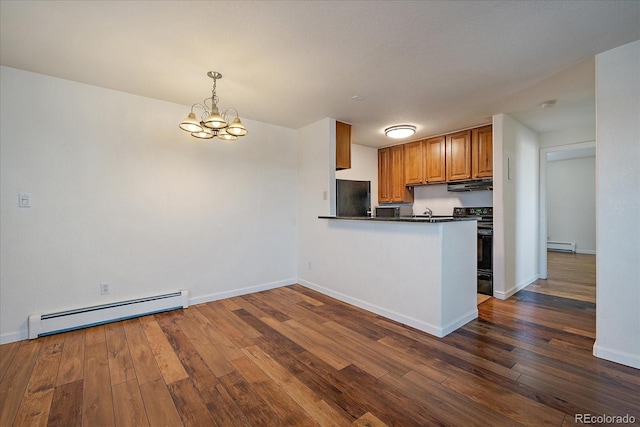 kitchen featuring dark countertops, dark wood-type flooring, under cabinet range hood, a baseboard radiator, and black refrigerator