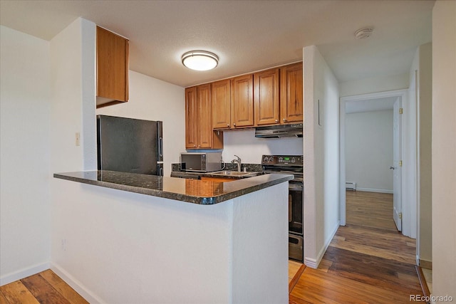 kitchen featuring a sink, freestanding refrigerator, wood finished floors, under cabinet range hood, and range with electric stovetop