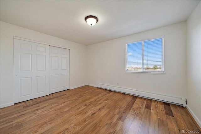 unfurnished bedroom with baseboards, baseboard heating, light wood finished floors, and a closet