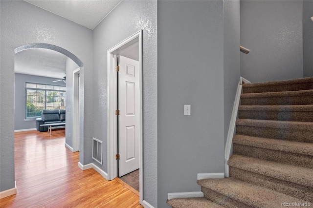 staircase with wood finished floors, baseboards, visible vents, arched walkways, and a textured wall