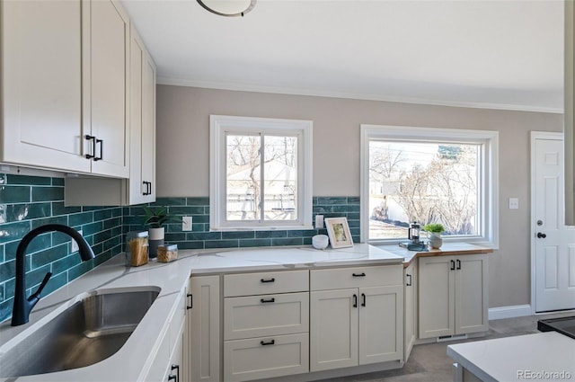 kitchen featuring light stone counters, backsplash, ornamental molding, and a sink