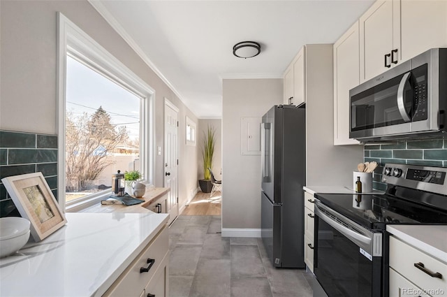 kitchen with backsplash, light countertops, ornamental molding, appliances with stainless steel finishes, and white cabinets