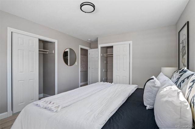 bedroom featuring baseboards, multiple closets, and wood finished floors