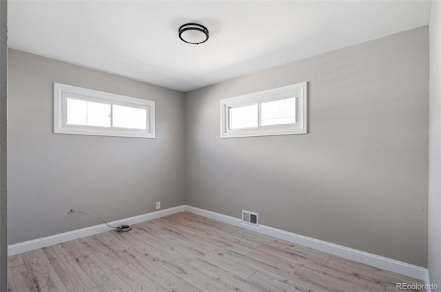 spare room featuring light wood-style floors, visible vents, and baseboards