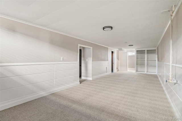 empty room featuring a wainscoted wall, built in shelves, carpet flooring, and crown molding