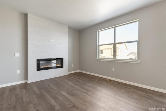 27746 E Byers Pl, Aurora, CO 80018 - unfurnished living room featuring a large fireplace, dark wood-style floors, and baseboards