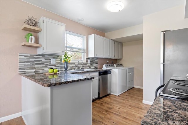 kitchen featuring stainless steel appliances, washer and clothes dryer, sink, dark stone countertops, and white cabinets