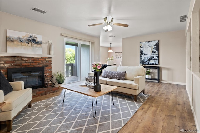 living room featuring ceiling fan, wood-type flooring, and a brick fireplace