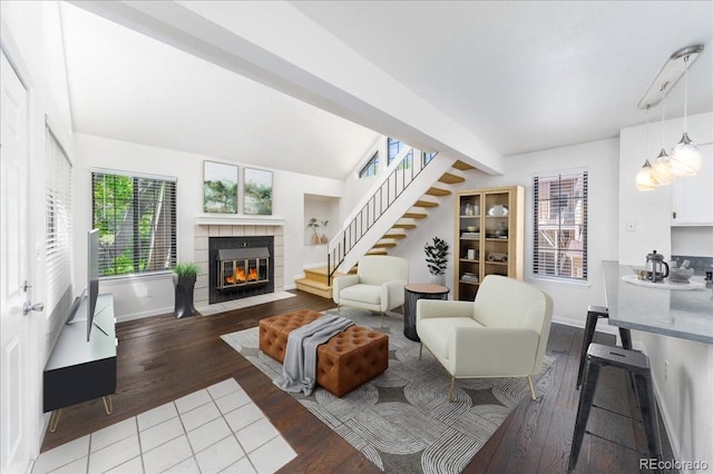 living room featuring stairway, a tile fireplace, lofted ceiling with beams, and hardwood / wood-style floors