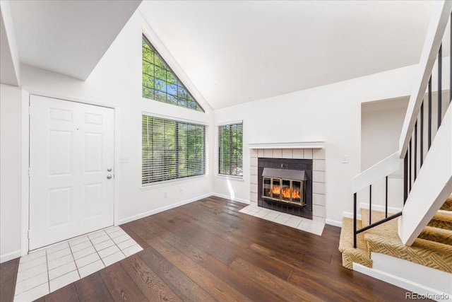 interior space featuring baseboards, high vaulted ceiling, stairs, hardwood / wood-style flooring, and a tiled fireplace