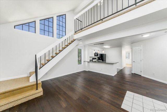 unfurnished living room featuring stairs, wood finished floors, baseboards, and a towering ceiling