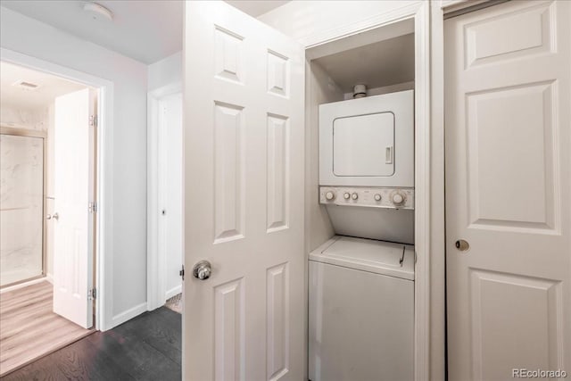 clothes washing area featuring baseboards, laundry area, dark wood-style flooring, and stacked washing maching and dryer