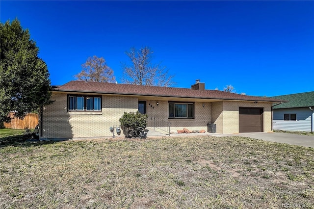 ranch-style house with a chimney, a garage, brick siding, a front lawn, and concrete driveway
