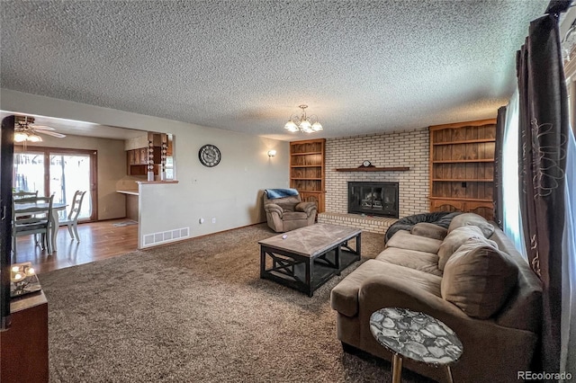 living room featuring a textured ceiling, visible vents, a fireplace, ceiling fan with notable chandelier, and carpet flooring