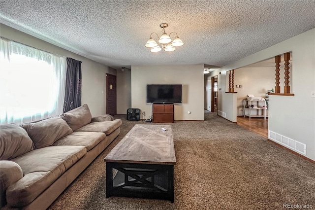 carpeted living room with baseboards, a textured ceiling, a chandelier, and visible vents
