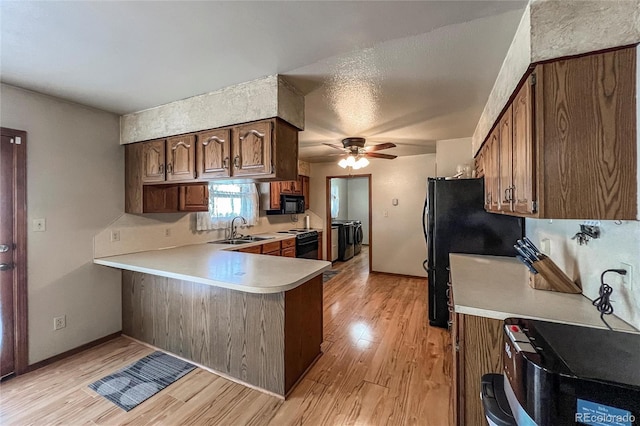 kitchen with washing machine and clothes dryer, a sink, light wood finished floors, light countertops, and black appliances