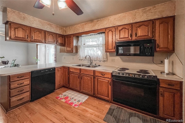 kitchen with brown cabinetry, light wood-style floors, ceiling fan, a sink, and black appliances