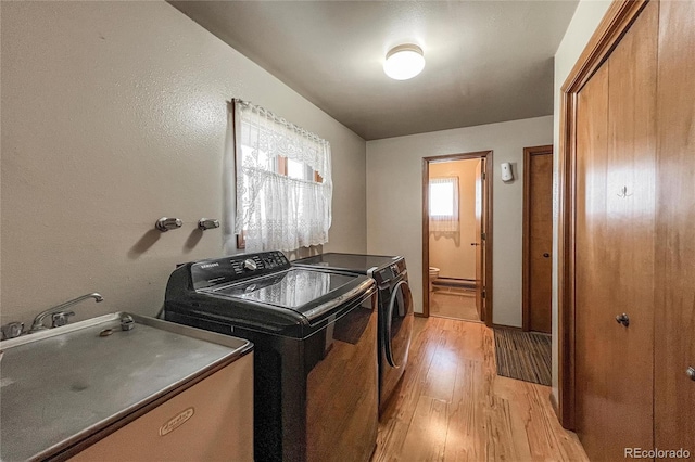 clothes washing area featuring a sink, laundry area, washing machine and dryer, and light wood finished floors