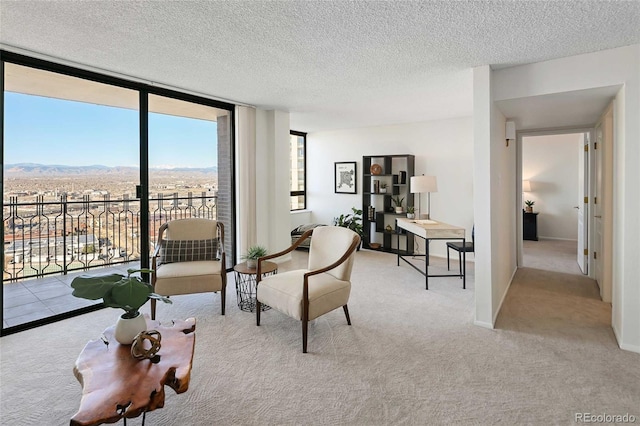 sitting room with carpet flooring, a mountain view, a textured ceiling, and a wall of windows