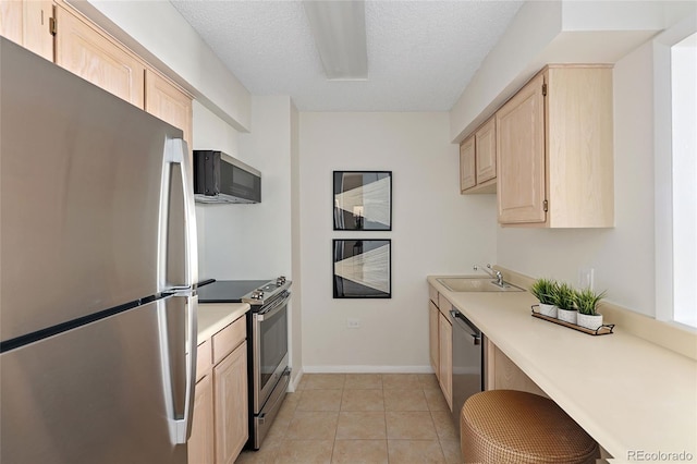 kitchen with a sink, appliances with stainless steel finishes, light brown cabinetry, and light countertops