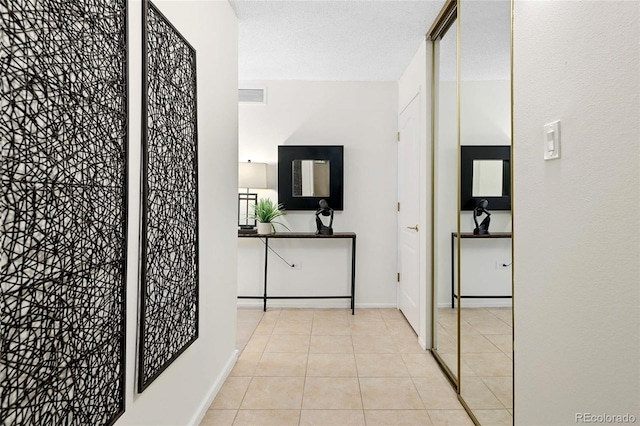 hallway featuring tile patterned floors, visible vents, baseboards, and a textured ceiling