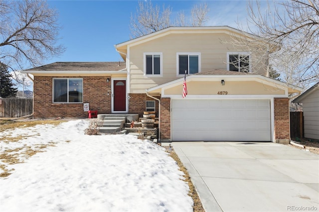 split level home featuring concrete driveway, brick siding, and fence