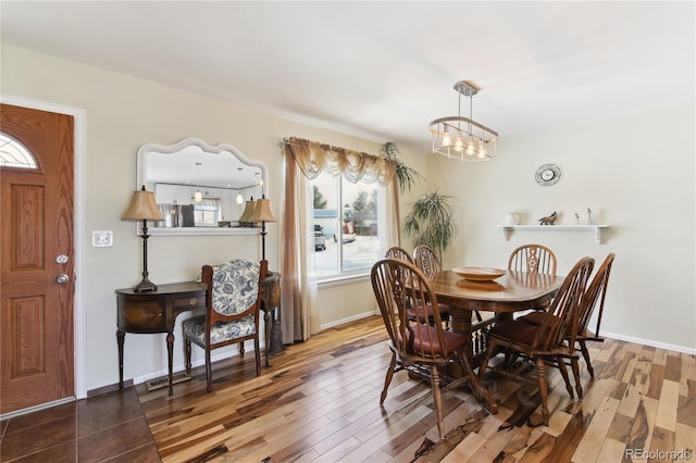 dining area featuring visible vents, a notable chandelier, baseboards, and wood finished floors