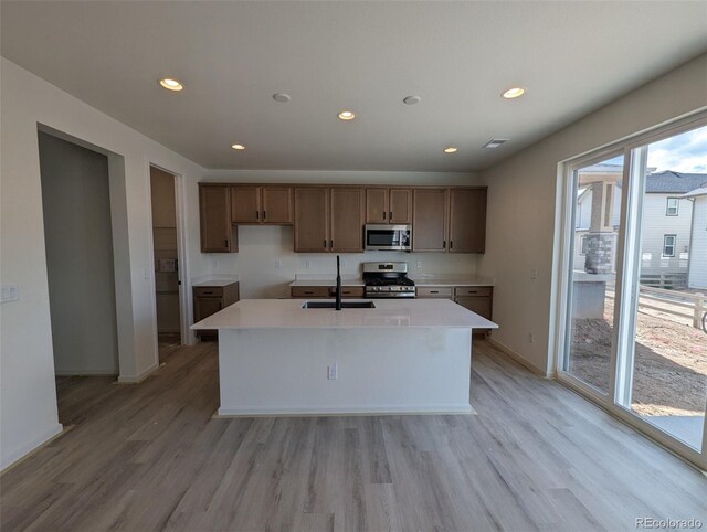 kitchen featuring appliances with stainless steel finishes, an island with sink, light wood-type flooring, and sink