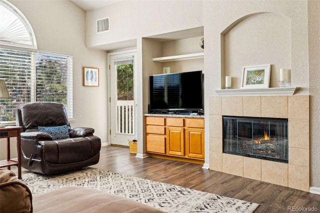 living area with built in features, baseboards, visible vents, dark wood finished floors, and a tiled fireplace