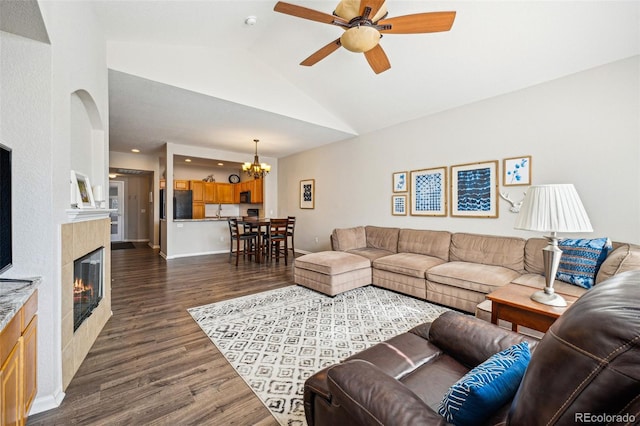 living room with dark wood-type flooring, baseboards, vaulted ceiling, ceiling fan with notable chandelier, and a glass covered fireplace