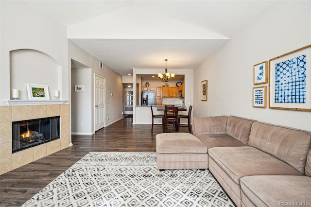 living area with visible vents, a notable chandelier, a tile fireplace, wood finished floors, and vaulted ceiling