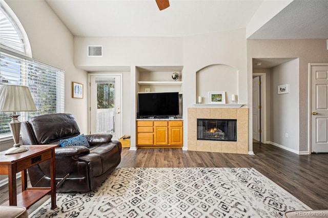 living area with visible vents, built in shelves, a tiled fireplace, wood finished floors, and baseboards