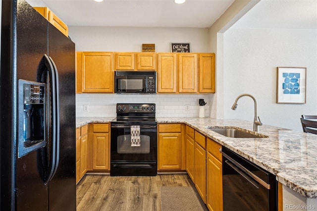 kitchen with light stone counters, wood finished floors, a sink, black appliances, and backsplash