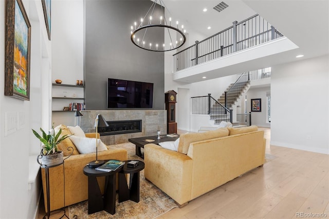 living room featuring a towering ceiling, a chandelier, wood finished floors, stairway, and a fireplace