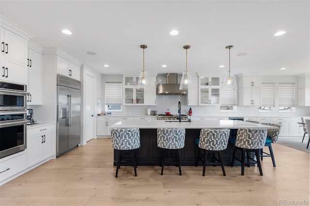kitchen featuring appliances with stainless steel finishes, wall chimney range hood, backsplash, light countertops, and recessed lighting
