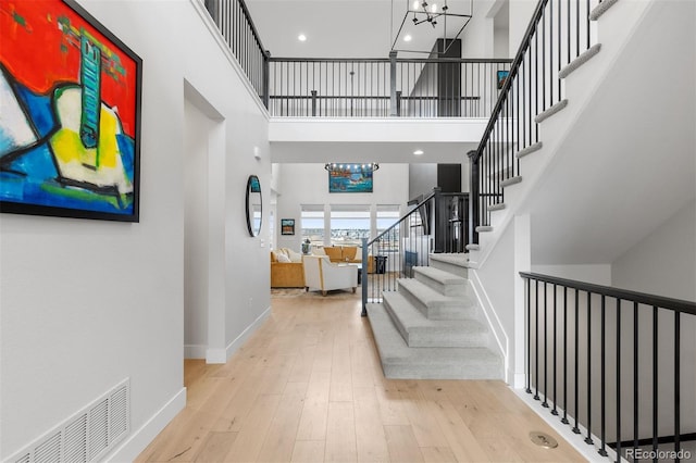 foyer entrance featuring hardwood / wood-style flooring, stairs, a chandelier, a high ceiling, and baseboards