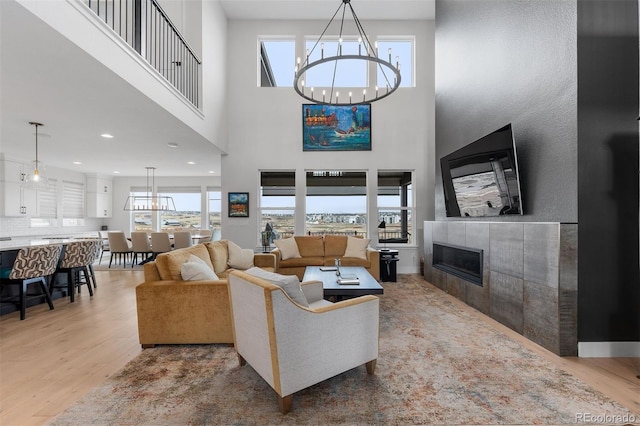 living area with plenty of natural light, a tiled fireplace, wood finished floors, and a notable chandelier