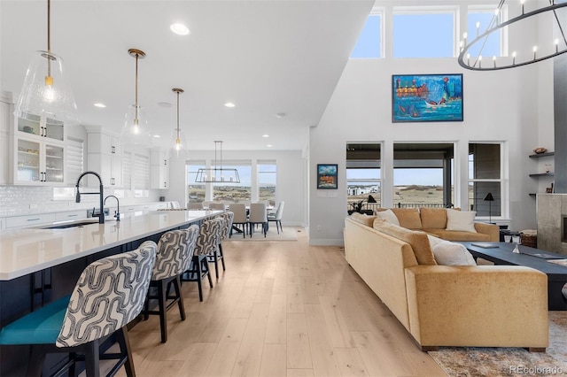 living area with light wood-style flooring, recessed lighting, baseboards, a chandelier, and a towering ceiling