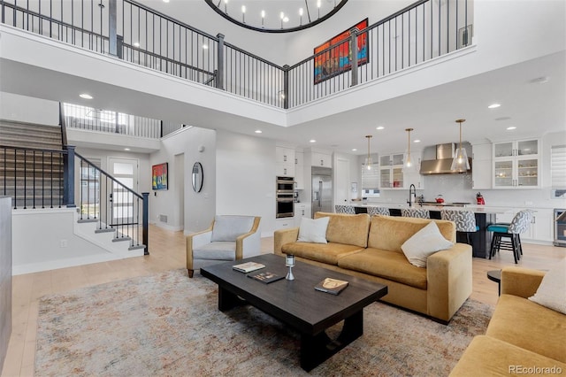 living room featuring light wood finished floors, a high ceiling, stairway, baseboards, and recessed lighting