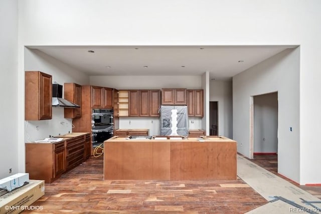 kitchen with stainless steel fridge, hardwood / wood-style flooring, an island with sink, wall chimney exhaust hood, and black double oven