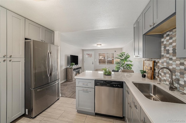 kitchen featuring stainless steel appliances, a peninsula, gray cabinetry, and a sink
