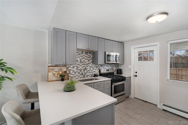 kitchen with stainless steel appliances, a sink, gray cabinets, baseboard heating, and light countertops