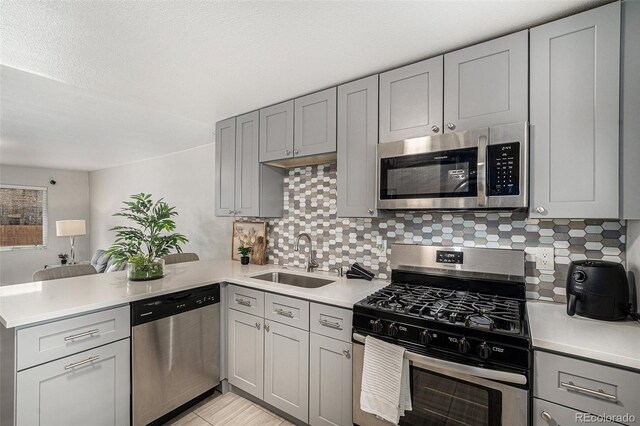 kitchen featuring a sink, a peninsula, light countertops, gray cabinetry, and appliances with stainless steel finishes