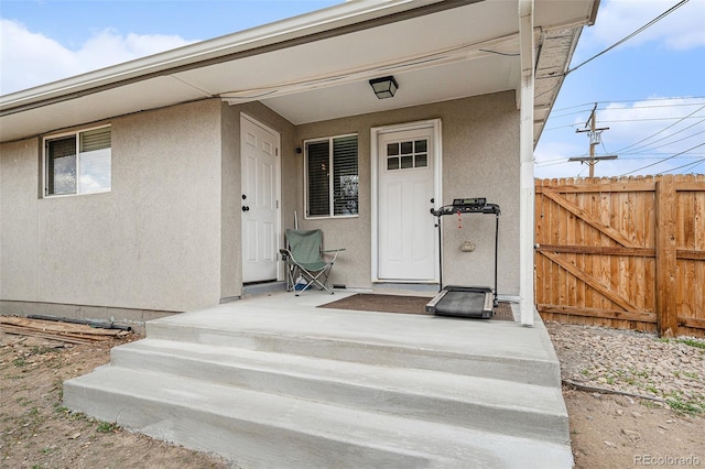 view of exterior entry featuring stucco siding, a gate, and fence