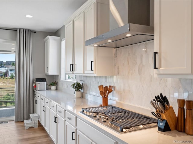 kitchen with white cabinetry, light wood-type flooring, wall chimney range hood, and stainless steel gas stovetop