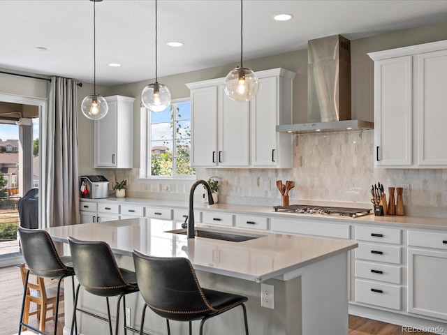 kitchen featuring decorative light fixtures, stainless steel gas cooktop, wall chimney exhaust hood, and a kitchen island with sink